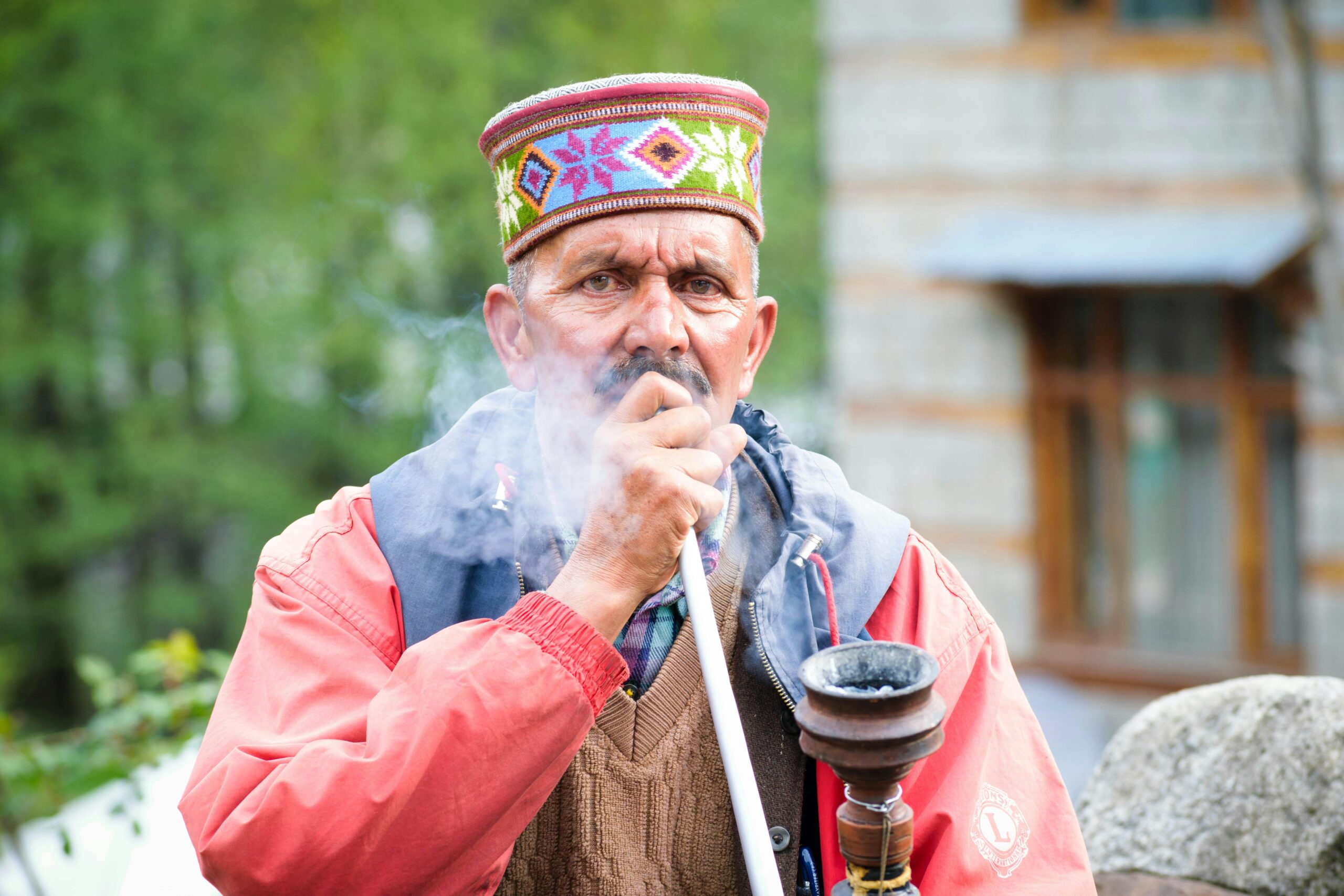 Elderly Himachali man in traditional attire smoking hookah outdoors in Manali.
